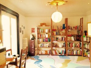 Sunny view of the library bookshelves, filled of colorful books. Pastel painted floor and office area with printer in the corner. 